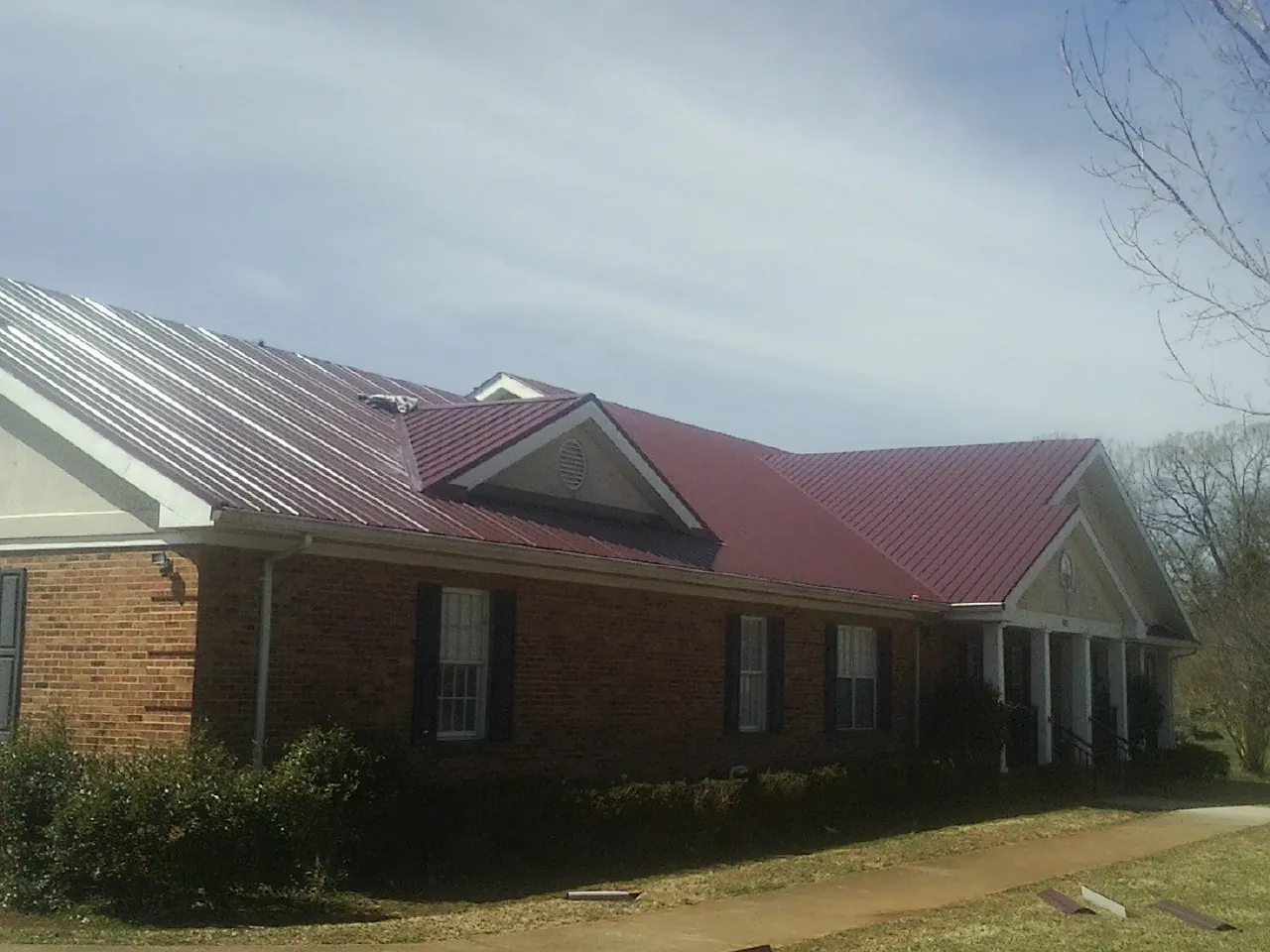 Red metal roof with gabled entries on a long brick building, from a Hail Damage Roof Repair job in Beltsville