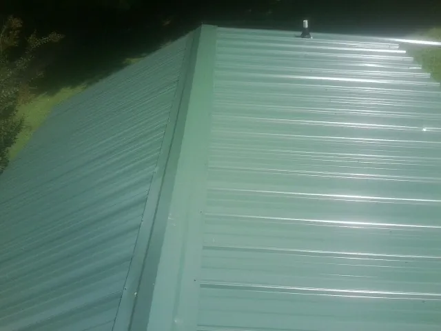 New green metal panels meeting at the ridge of a roof — Flat Roof Repair work by our crew in Beltsville