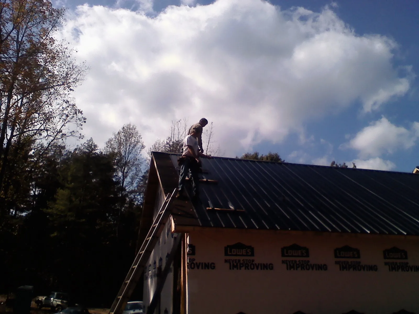 Roofer fastening dark metal panels high against a cloudy sky, from a Roof Inspection job in Beltsville
