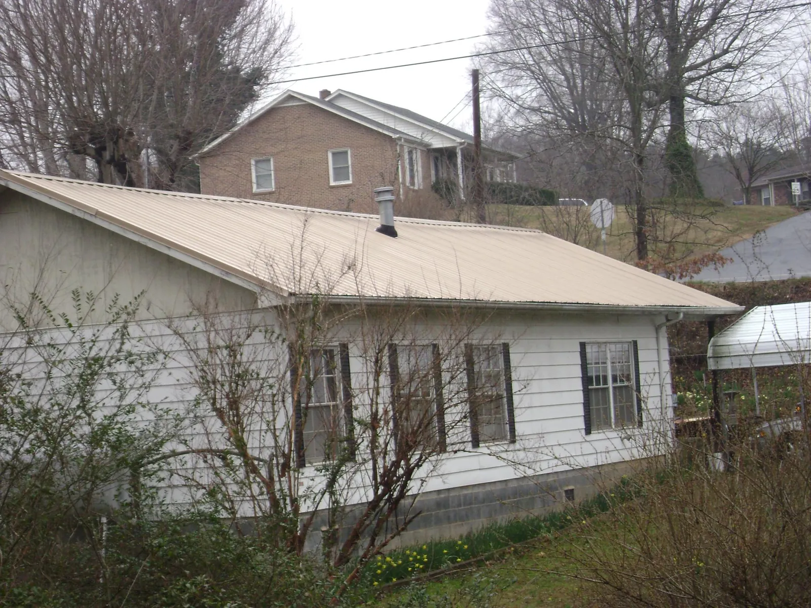 Tan metal roof on a white sided house set into a hillside — Commercial Roofing by Roofing Brothers in Beltsville